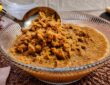 Doce de ambrosia cremoso e grumoso em calda de caramelo em uma tigela de vidro com concha de servir.