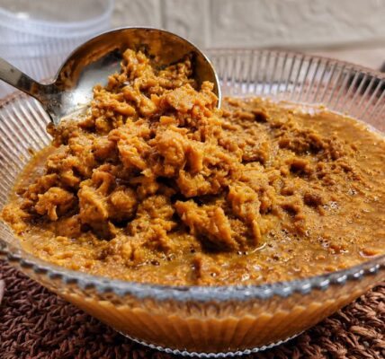 Doce de ambrosia cremoso e grumoso em calda de caramelo em uma tigela de vidro com concha de servir.