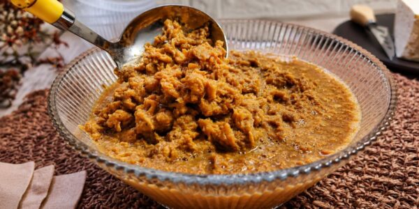 Doce de ambrosia cremoso e grumoso em calda de caramelo em uma tigela de vidro com concha de servir.