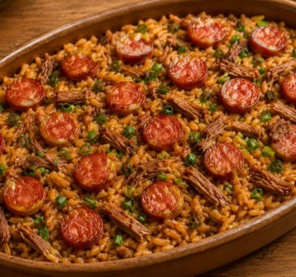 Uma assadeira de barro oval repleta de arroz de pato português, coberto com rodelas douradas de linguiça, carne de pato desfiada e cebolinha fresca picada sobre uma mesa de madeira rústica.