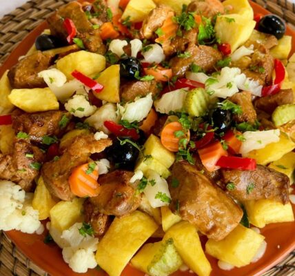 Prato tradicional de carne de porco à portuguesa servido em travessa de barro com cubos de batata assada, pickles variados, azeitonas pretas e coentros picados.