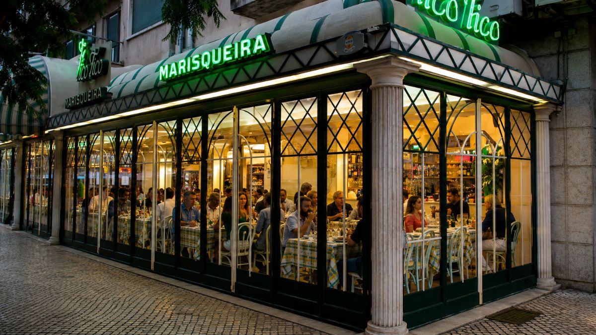Fachada iluminada da marisqueira Tico Tico com grande salão envidraçado e clientes jantando em mesas postas na zona de Alvalade em Lisboa.