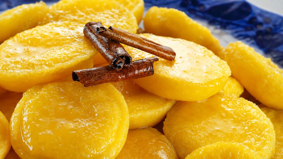Close em doces papos de anjo amarelos brilhantes imersos em calda transparente com canela em pau por cima sobre prato azul.
