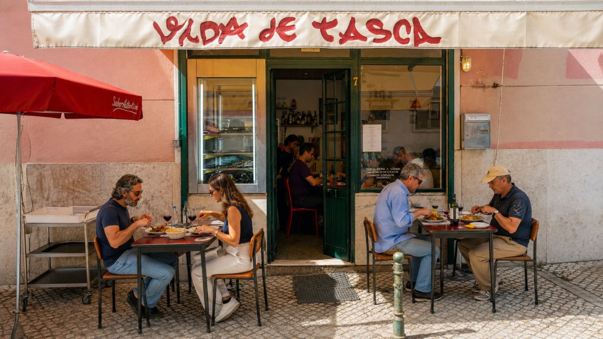 Fachada e esplanada do restaurante Vida de Tasca com clientes almoçando em mesas na calçada de calçada portuguesa em Lisboa.
