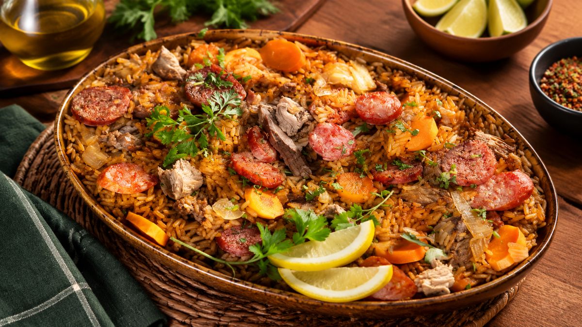 Tabuleiro oval de cerâmica com arroz de pato tradicional no forno, decorado com rodelas de chouriço tostadas, rodelas de cenoura, salsa fresca e fatias de limão.