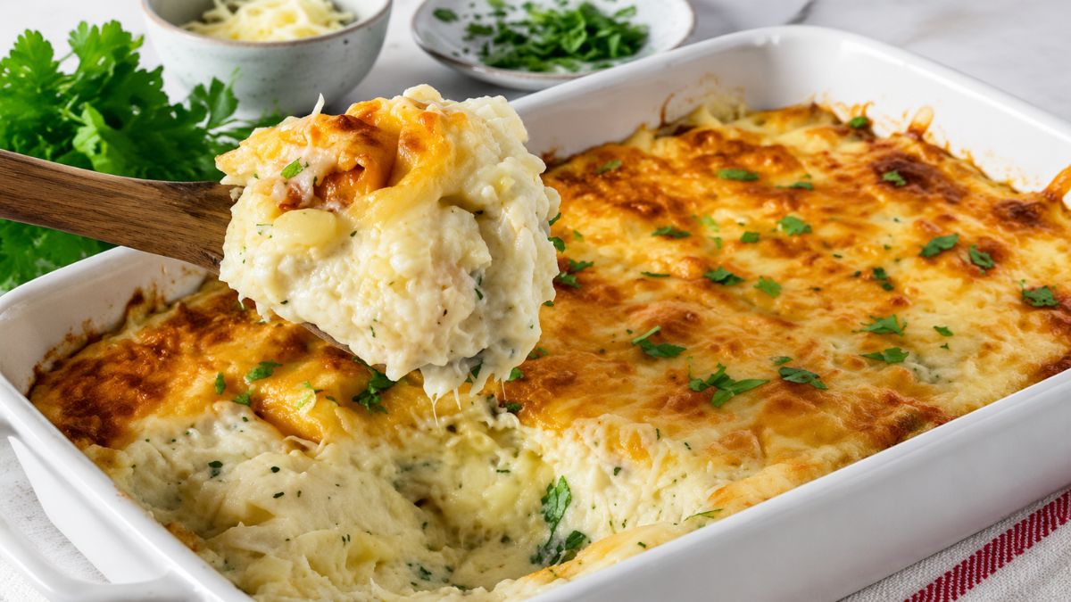 Tabuleiro de assar branco com Bacalhau à Conde da Guarda cremoso, coberto por queijo bem gratinado e dourado, com uma colher de pau a retirar uma porção generosa do prato.