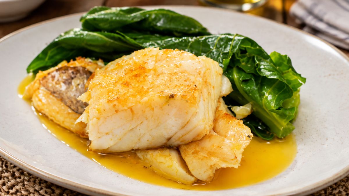 Lombo de bacalhau cozido servido com couves verdes e regado com azeite num prato fundo de cerâmica.