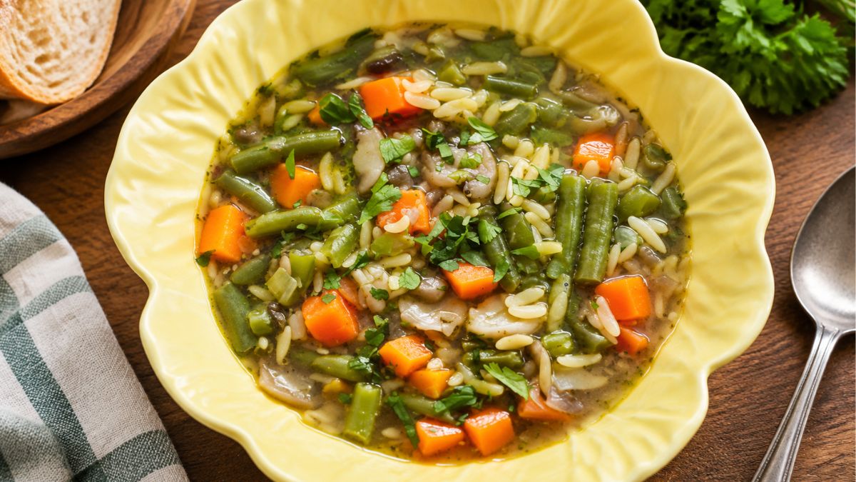 Uma imagem do topo mostra uma sopa rica e vegetariana de cogumelos e feijão-verde, numa taça amarela em forma de folha, com pedaços visíveis de cenoura, orzo e ervas frescas, ao lado de pão e uma colher numa mesa de madeira rústica.
