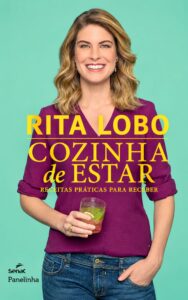 A apresentadora de televisão e chef de cozinha Rita Lobo sorri para a câmera com uma blusa roxa, jeans e segurando uma bebida com lima na mão. Sobre a imagem dela está o título do livro Cozinha de Estar. O subtítulo Receitas Práticas para Receber e o logotipo do Senac Panelinha também são visíveis.