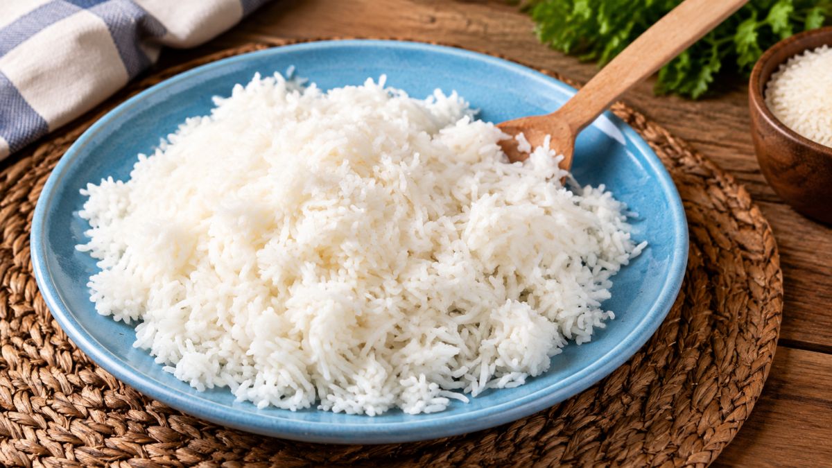 Prato azul com arroz basmati branco e solto servido com uma colher de pau sobre uma mesa de madeira rustica.