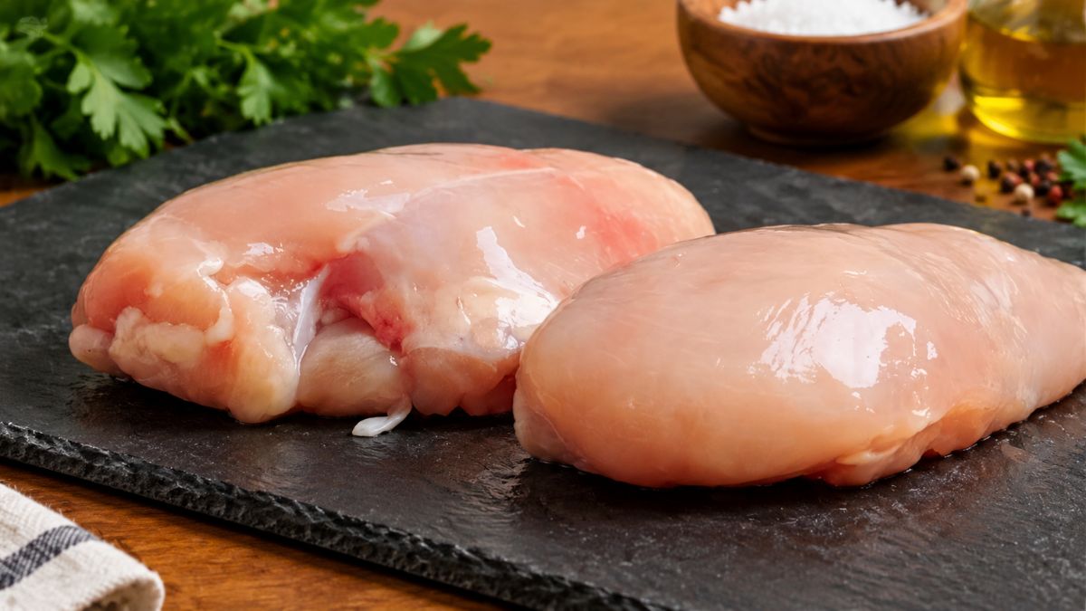 Fotografia de dois peitos de frango crus e frescos dispostos sobre uma tábua de xisto preta, prontos para cozinhar.