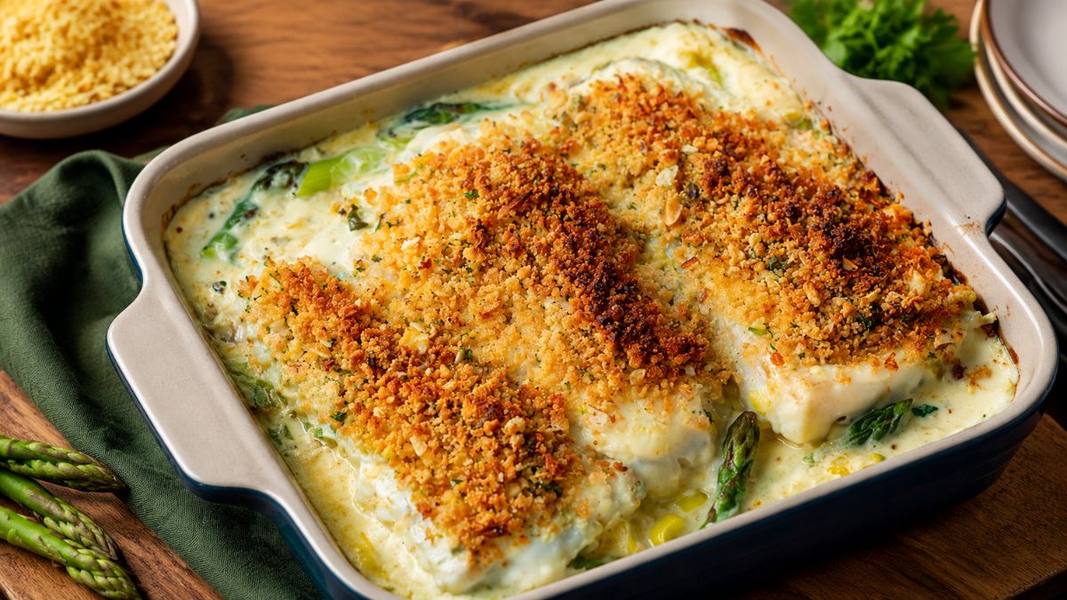 Prato de assadeira com lombos de bacalhau envoltos em molho cremoso, espargos verdes e coberto por uma camada crocante de crumble dourado de pão e frutos secos.