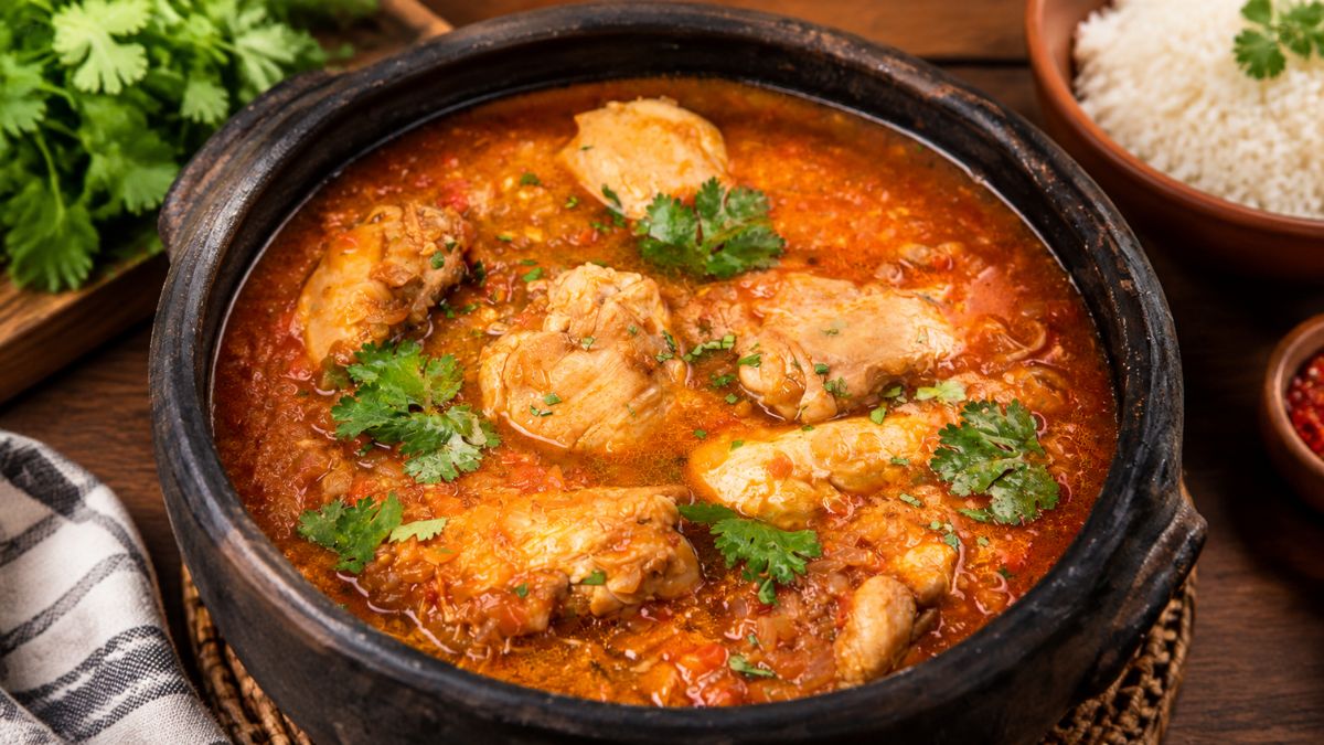Suculento frango cozido servido numa panela de barro com caldo aromático e ervas frescas.
