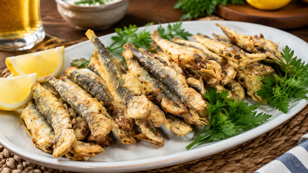 Travessa branca servida com petingas fritas bem douradas, acompanhadas por gomos de limão fresco e folhas de salsa verde.