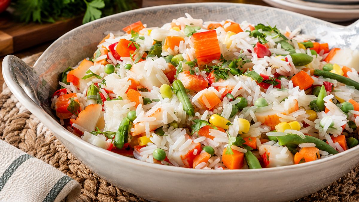 Arroz de legumes com delícias do mar em tigela de cerâmica rústica, misturado com macedónia de cenoura, ervilhas, milho e feijão verde, e salsa picada, pronto para servir.