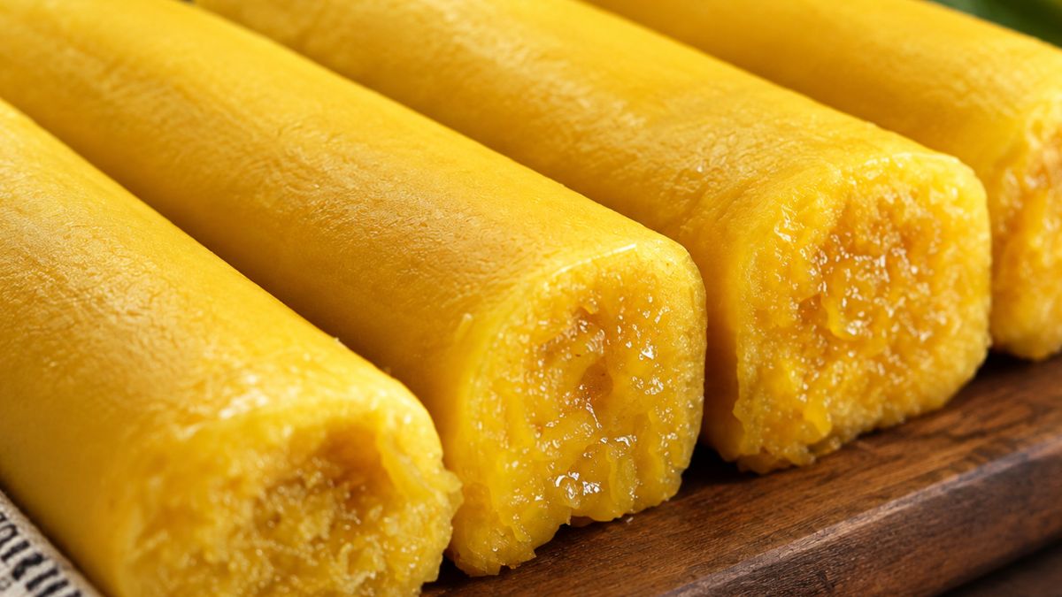 Fotografia em plano aproximado de fatias de torta de Azeitão enroladas com massa dourada e recheio cremoso de doce de gema sobre uma tábua de madeira.