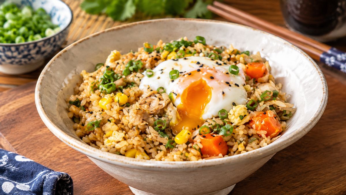 Tigela de arroz xau xau salteado com legumes da horta, milho doce e ovo, coberto por um ovo escalfado de gema cremosa e polvilhado com cebolinha e sésamo preto.