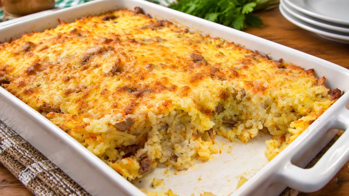Arroz de frango com queijo parmesão gratinado e dourado servido numa assadeira retangular de cerâmica branca sobre mesa de madeira.