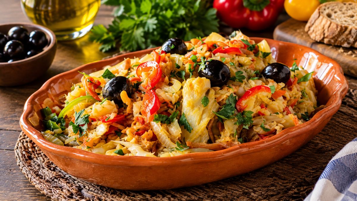 Bacalhau à Assis servido numa travessa de barro tradicional com lascas de bacalhau, batata palha, pimentos vermelhos, cebola, ovos e azeitonas pretas polvilhado com salsa fresca.