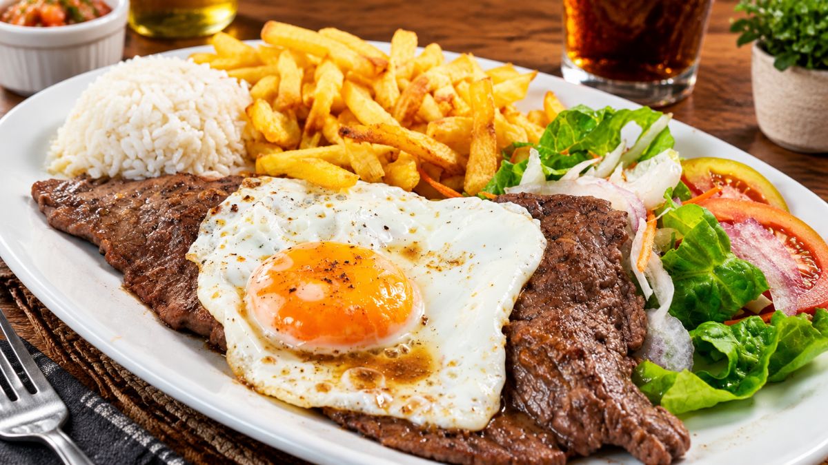 Um prato de bitoque tradicional português servido com bife de vaca, ovo estrelado a cavalo, batatas fritas crocantes, arroz branco e salada mista.