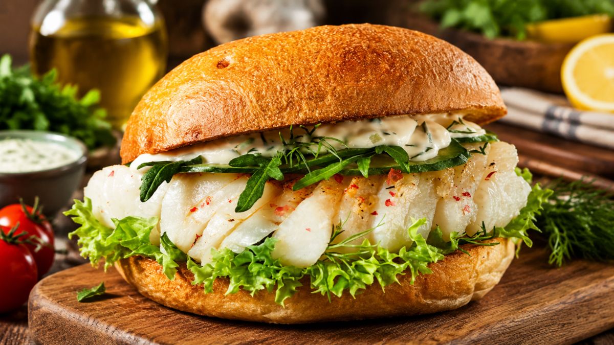 Hambúrguer de bacalhau sucilento servido em pão rústico dourado com molho cremoso de ervas, folhas de rúcula e alface fresca.