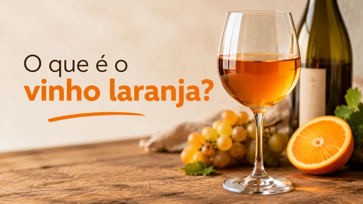 Copo com vinho laranja sobre mesa de madeira com garrafa, uvas brancas e rodela de laranja ao lado.
