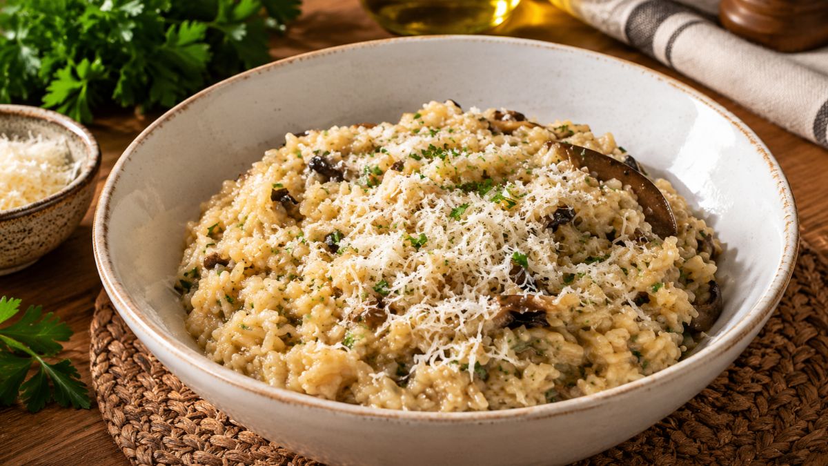 Tigela de risoto de cogumelos cremoso coberto com queijo parmesão ralado e salsa verde picada em uma mesa de madeira rústica.
